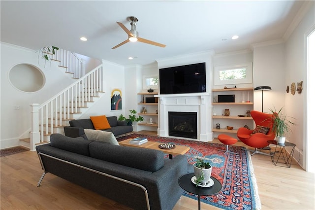 living area featuring a fireplace, stairway, wood finished floors, and ornamental molding