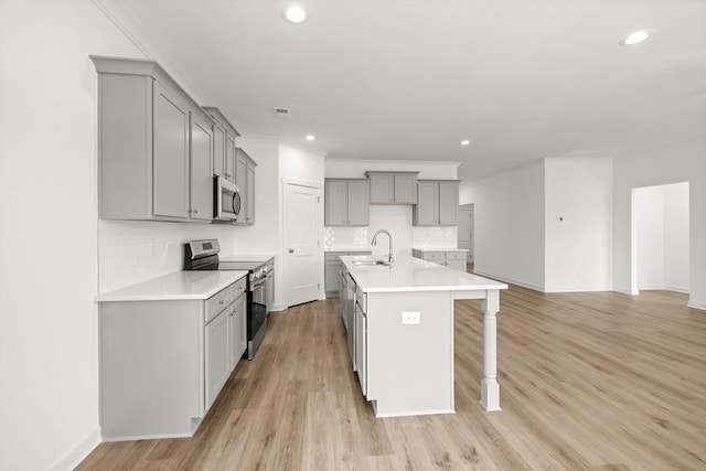 kitchen with stainless steel appliances, light wood-style flooring, gray cabinetry, a kitchen island with sink, and a kitchen bar