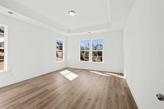 empty room featuring baseboards, visible vents, a tray ceiling, and wood finished floors