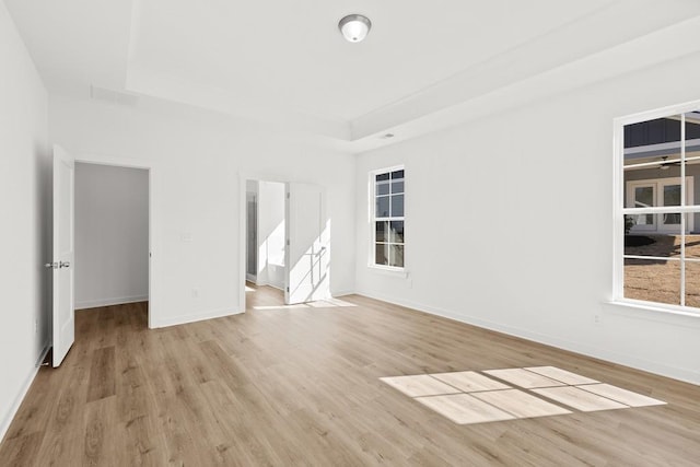 empty room featuring light wood-style floors, baseboards, and a raised ceiling