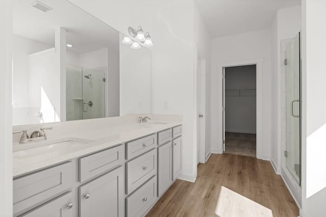 bathroom featuring visible vents, a spacious closet, a sink, a shower stall, and wood finished floors