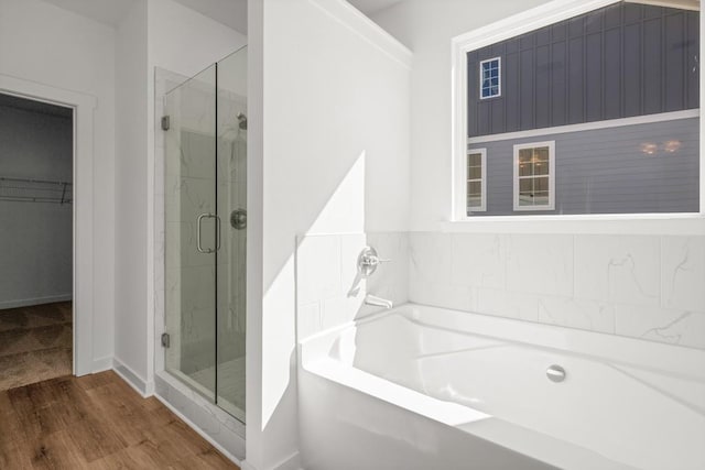 bathroom with a garden tub, a shower stall, a walk in closet, and wood finished floors