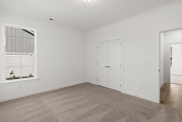 unfurnished bedroom featuring baseboards, a closet, carpet flooring, and crown molding