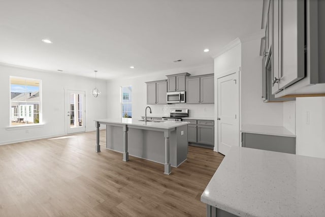 kitchen with stainless steel appliances, gray cabinets, a sink, wood finished floors, and a kitchen bar