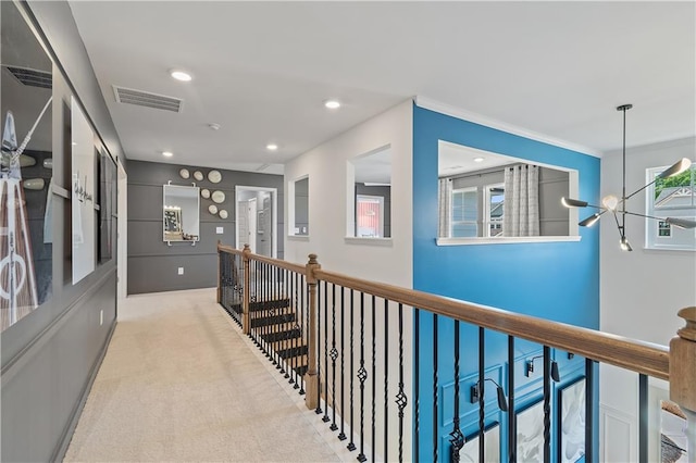 hall with a chandelier, crown molding, and light colored carpet