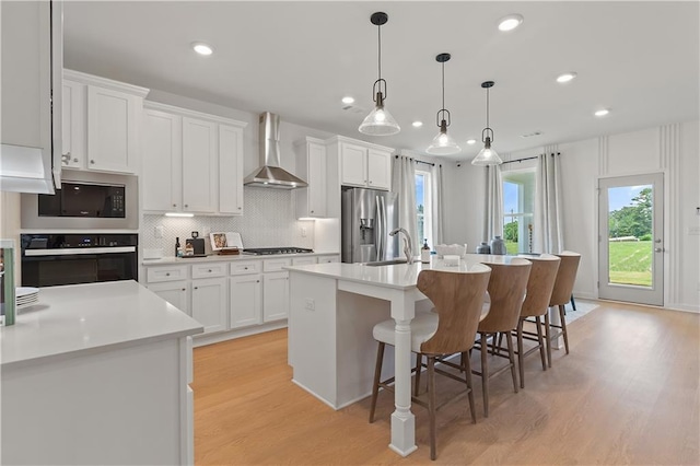 kitchen with an island with sink, white cabinets, appliances with stainless steel finishes, and wall chimney range hood