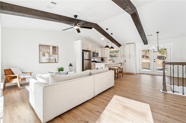 living room with vaulted ceiling with beams, ceiling fan with notable chandelier, and light hardwood / wood-style floors