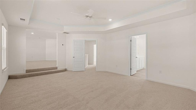 unfurnished room with a tray ceiling, ceiling fan, crown molding, and light carpet