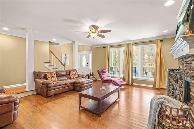 living area with a ceiling fan, wood finished floors, a fireplace, decorative columns, and stairs