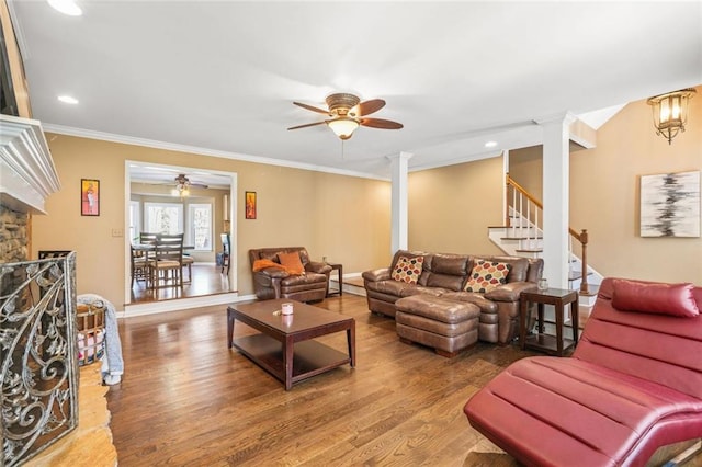 living area with crown molding, stairway, decorative columns, a stone fireplace, and wood finished floors