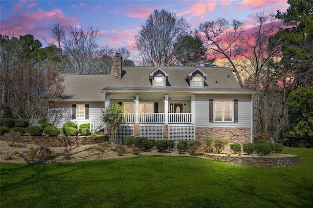 view of front of property featuring a chimney, stone siding, covered porch, and a front lawn