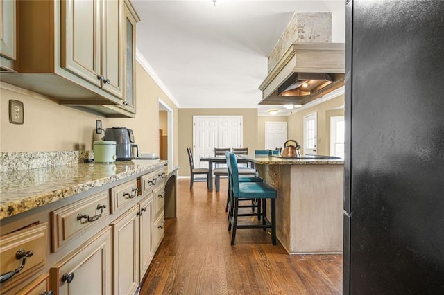 kitchen featuring light stone counters, dark wood-style floors, freestanding refrigerator, ornamental molding, and a kitchen breakfast bar