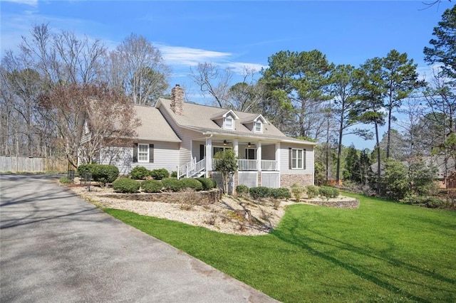 cape cod home with ceiling fan, a porch, a front yard, a chimney, and stone siding