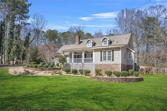 view of front facade with a ceiling fan, stone siding, covered porch, a front yard, and a chimney