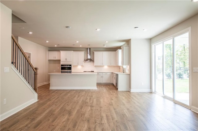 kitchen with light hardwood / wood-style flooring, appliances with stainless steel finishes, white cabinets, a center island, and wall chimney range hood