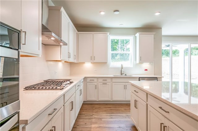 kitchen with sink, white cabinets, stainless steel gas stovetop, and wall chimney exhaust hood