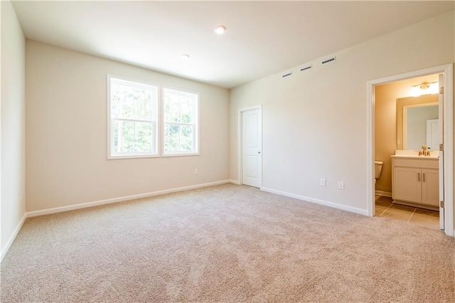 unfurnished bedroom featuring ensuite bathroom and light carpet