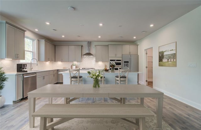 kitchen with wall chimney range hood, appliances with stainless steel finishes, gray cabinetry, and a kitchen island