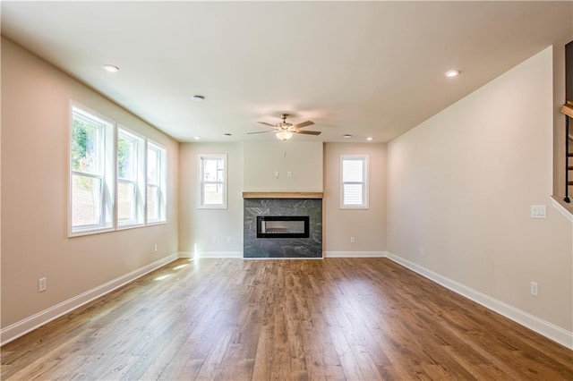 unfurnished living room featuring ceiling fan, hardwood / wood-style floors, and a high end fireplace