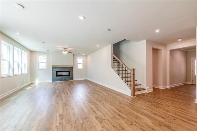 unfurnished living room with ceiling fan, light hardwood / wood-style floors, and a tiled fireplace