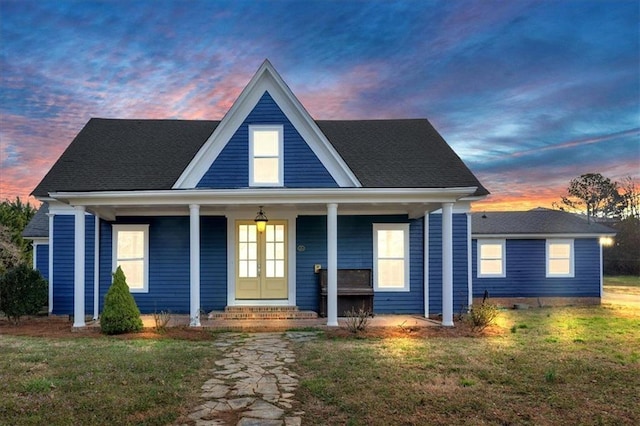 view of front facade featuring a shingled roof, french doors, covered porch, and a lawn