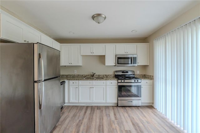 kitchen with sink, light wood-type flooring, white cabinetry, light stone counters, and stainless steel appliances