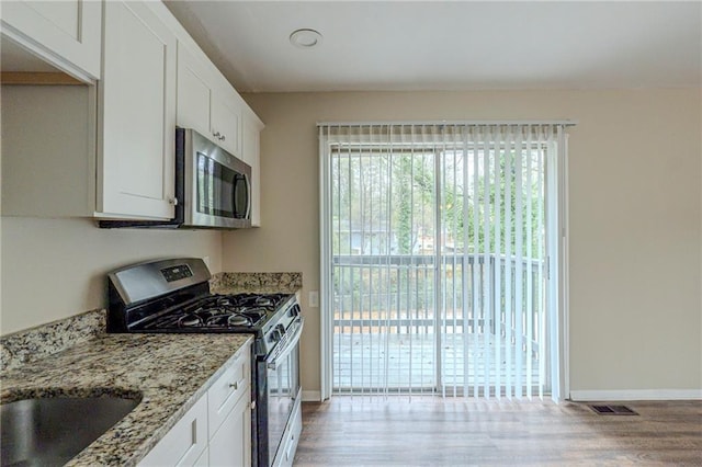 kitchen with white cabinets, stainless steel appliances, light stone counters, and light hardwood / wood-style floors