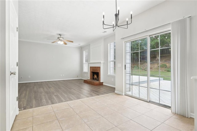 unfurnished living room with a fireplace, baseboards, ceiling fan with notable chandelier, and light wood-style floors