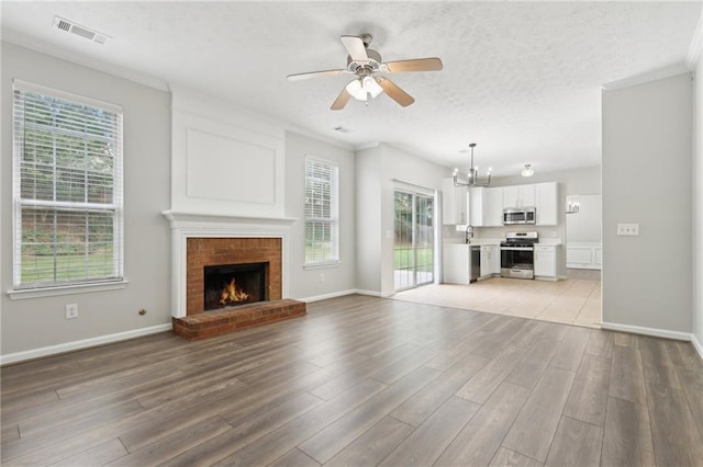 unfurnished living room with ceiling fan with notable chandelier, light wood finished floors, a brick fireplace, and visible vents