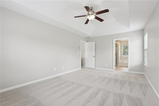 unfurnished bedroom with ceiling fan, light carpet, a raised ceiling, baseboards, and ensuite bathroom