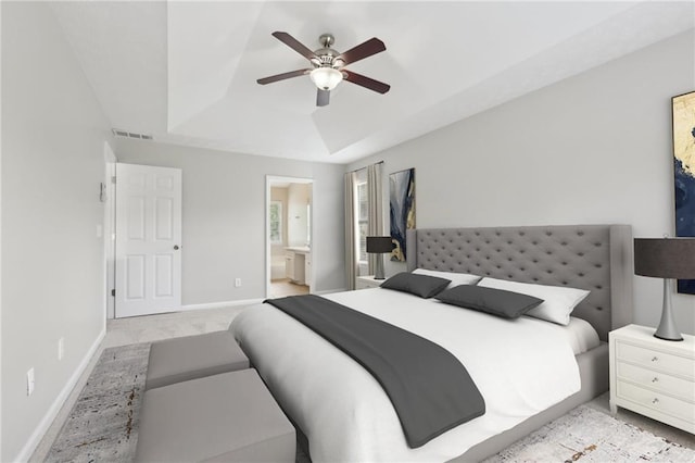 bedroom featuring a ceiling fan, visible vents, baseboards, ensuite bathroom, and a tray ceiling