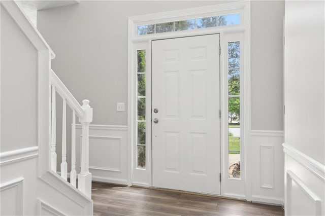 entrance foyer with stairs, a decorative wall, wood finished floors, and a wainscoted wall