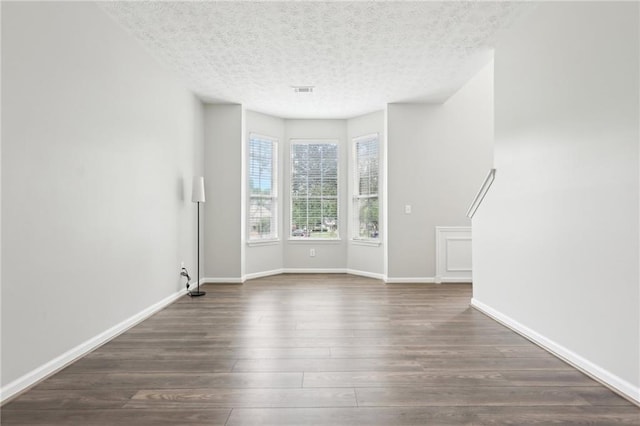 unfurnished living room with baseboards, dark wood-style flooring, and a textured ceiling
