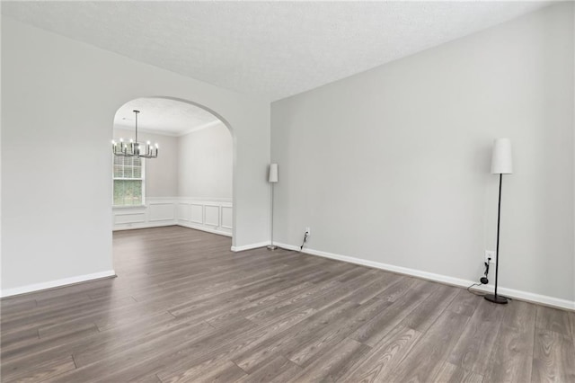 empty room with ornamental molding, baseboards, arched walkways, dark wood finished floors, and a notable chandelier