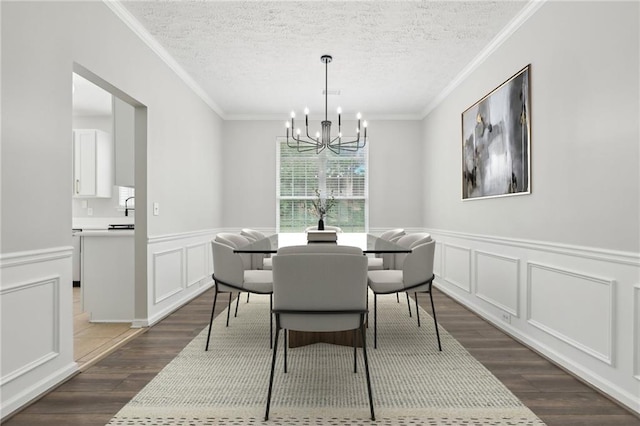 dining room featuring a notable chandelier, a decorative wall, a textured ceiling, a wainscoted wall, and dark wood-style floors