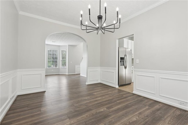 unfurnished dining area featuring an inviting chandelier, wainscoting, arched walkways, a textured ceiling, and dark wood-type flooring