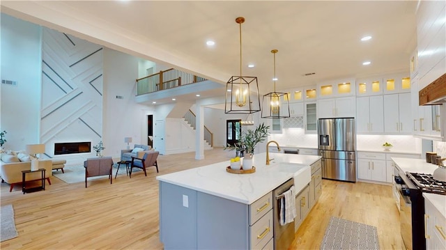 kitchen with white cabinets, a center island with sink, glass insert cabinets, and stainless steel appliances