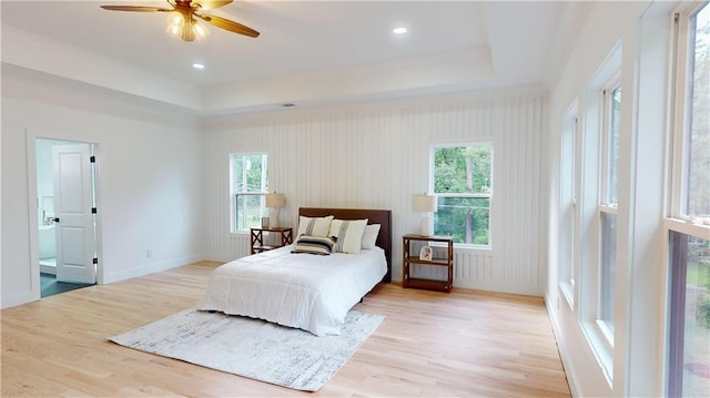 bedroom featuring light wood-type flooring, baseboards, multiple windows, and a tray ceiling