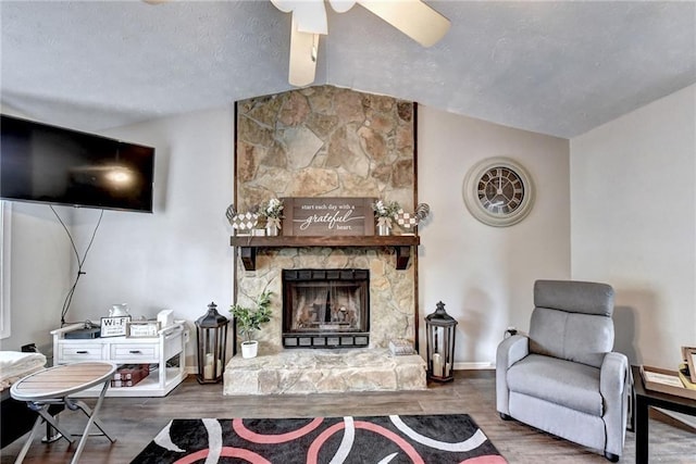 living room with dark wood-type flooring, ceiling fan, a fireplace, and vaulted ceiling