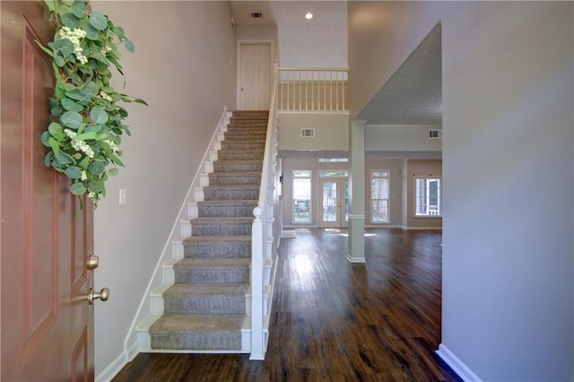 foyer entrance featuring dark wood-style floors, stairway, baseboards, and a towering ceiling