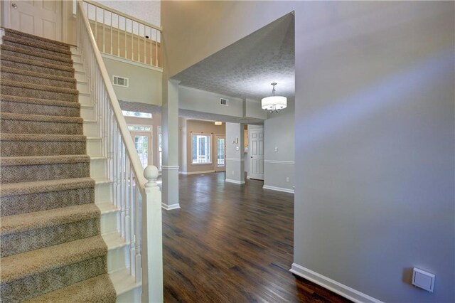 stairway featuring an inviting chandelier, a textured ceiling, dark hardwood / wood-style floors, and a high ceiling