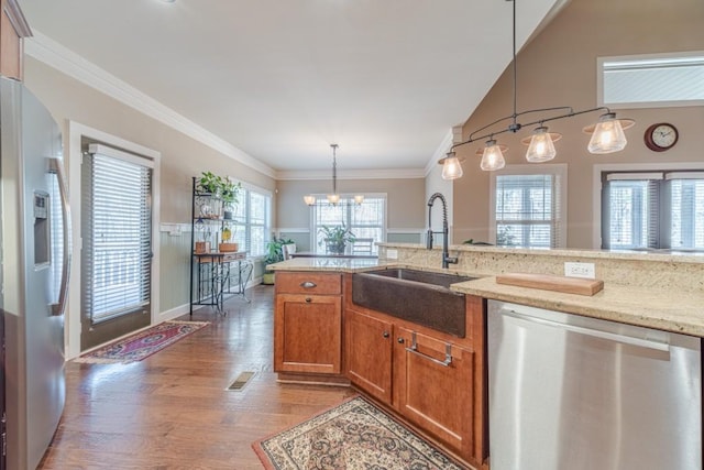 kitchen featuring brown cabinetry, light stone counters, a sink, light wood finished floors, and appliances with stainless steel finishes