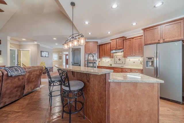kitchen with ornamental molding, a kitchen breakfast bar, light wood-type flooring, under cabinet range hood, and stainless steel appliances