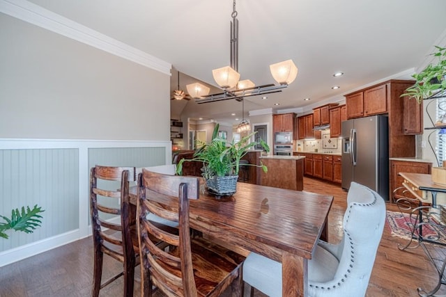 dining room with ornamental molding, wainscoting, a decorative wall, light wood-style floors, and a notable chandelier