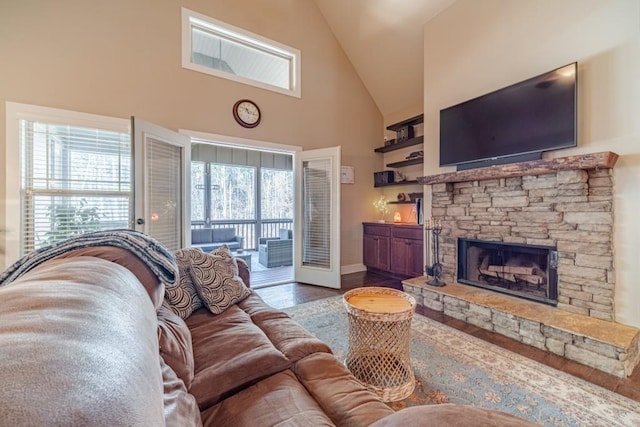 living room featuring high vaulted ceiling, baseboards, a stone fireplace, and wood finished floors