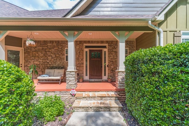 doorway to property with a shingled roof, board and batten siding, covered porch, and stone siding