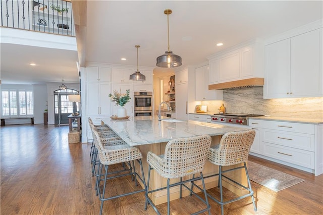 kitchen with wood finished floors, a sink, white cabinetry, appliances with stainless steel finishes, and backsplash