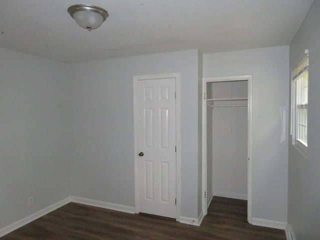 unfurnished bedroom featuring dark wood-type flooring, multiple windows, and a closet