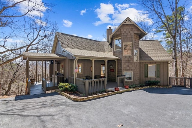 rustic home featuring covered porch, a chimney, and roof with shingles