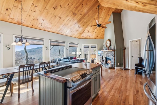 kitchen with light wood-type flooring, high vaulted ceiling, stainless steel appliances, a stone fireplace, and wooden ceiling